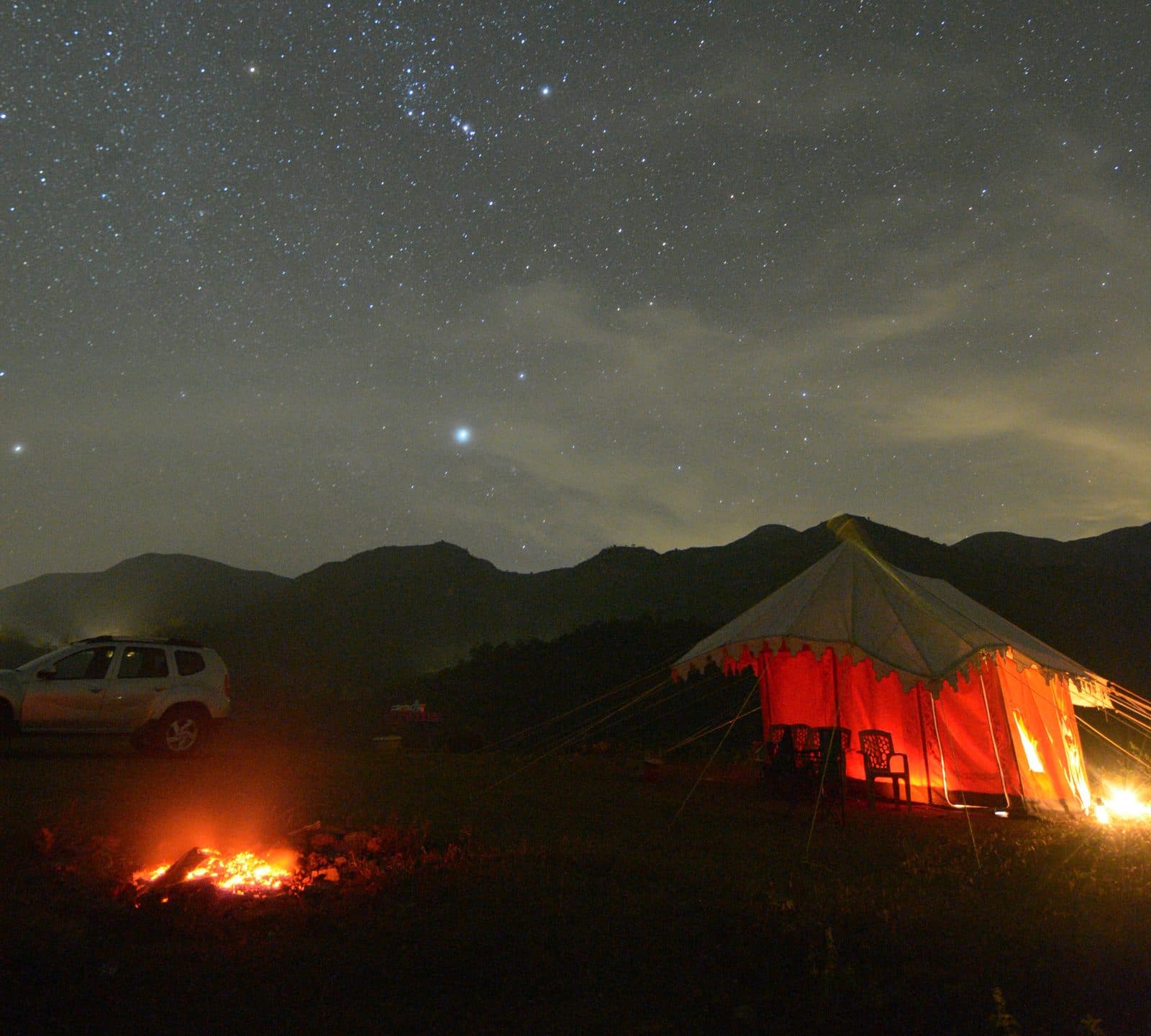 Campfire glowing beside a tent under a starry night sky